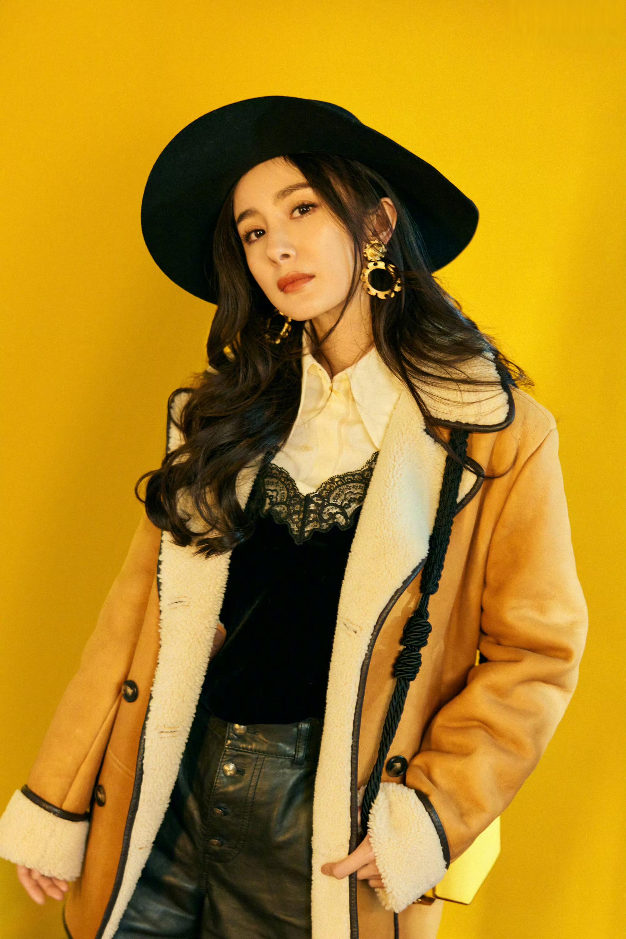 杨幂幂优雅地站在阳光下,身穿棕色外套,头戴黑色帽子,手持黄色包包,脚